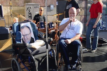 Bild från Mynttorget; slutet på Marschen för tillgänglighet 2004: Göran Perssons stand in - ett foto av GP uppsatt i en rullstol - har just mottagit listan med namnunderskrifter utskrivna med både punktskrift och vanlig skrift av Hans Filipsson, marschens koordinator. Bild från Mynttorget; slutet på Marschen för tillgänglighet 2004: Göran Perssons stand in - ett foto av GP uppsatt i en rullstol - har just mottagit listan med namnunderskrifter utskrivna med både punktskrift och vanlig skrift av Hans Filipsson, marschens koordinator.